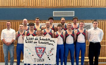 Turnteam des TSV Friedrichsort mit Banner beim Wettkampf, gruppiert in der Sporthalle für ein Teamfoto.