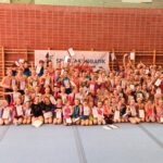 Große Gruppe junger Sportakrobat*innen posiert mit Urkunden und Medaillen in der Turnhalle.