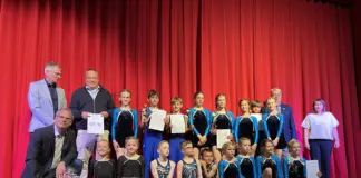 Turngruppe bei Ehrung auf Bühne mit Urkunden, Pokalen und rotem Vorhang