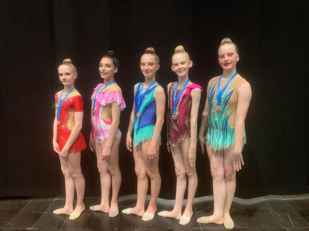 Fünf Personen in Gymnastikanzügen mit Medaillen um den Hals stehen nebeneinander
