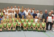 Eine Gruppe von Menschen in Sportkleidung posiert für ein Gruppenfoto in einer Turnhalle.
