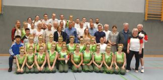 Eine Gruppe von Menschen in Sportkleidung posiert für ein Gruppenfoto in einer Turnhalle.