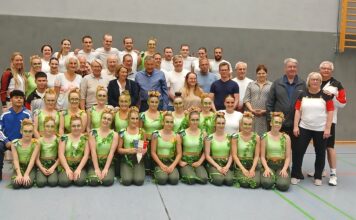 Eine Gruppe von Menschen in Sportkleidung posiert für ein Gruppenfoto in einer Turnhalle.