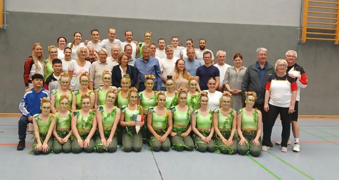 Eine Gruppe von Menschen in Sportkleidung posiert für ein Gruppenfoto in einer Turnhalle.