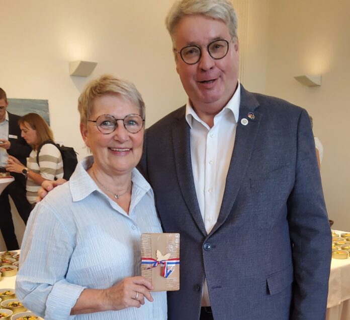 Zwei Personen stehen nebeneinander, eine davon hält ein Geschenk in der Hand.