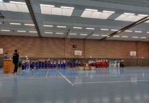 Gruppe von Sportlern in Uniformen steht in einer Turnhalle.