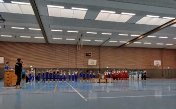 Gruppe von Sportlern in Uniformen steht in einer Turnhalle.