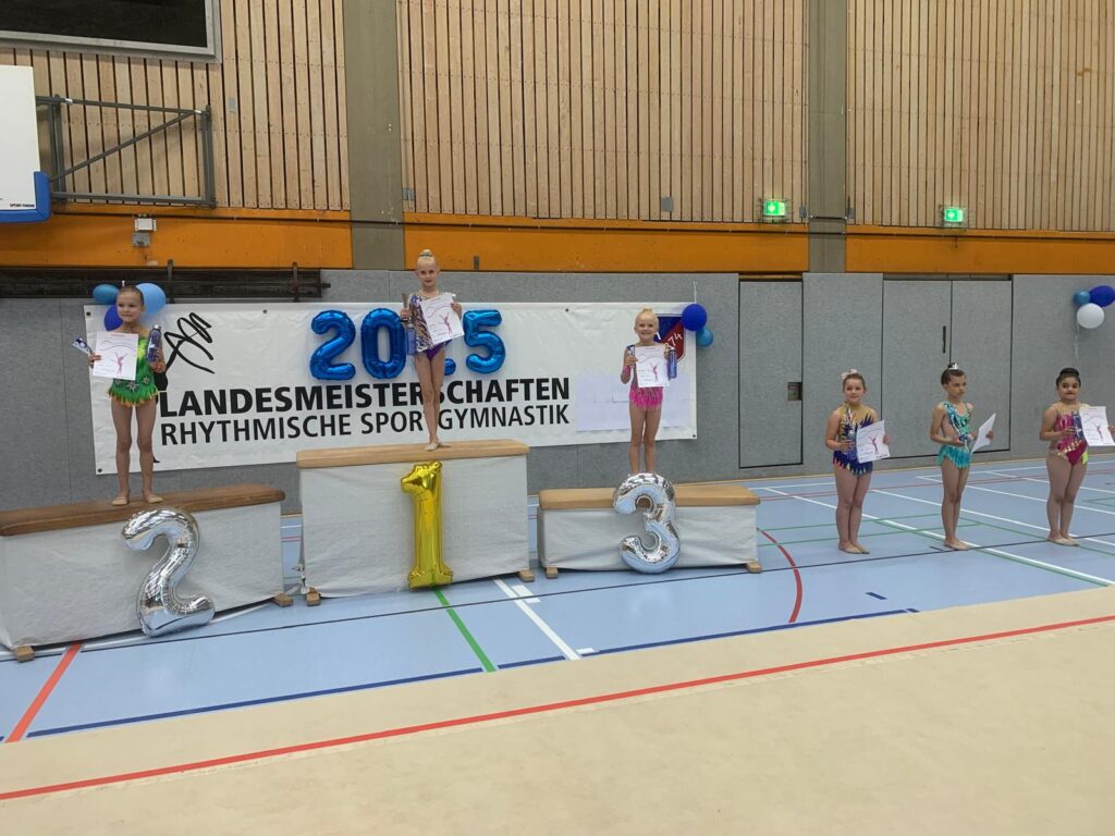 Siegerehrung bei einem Turnwettbewerb mit Podestplätzen und Teilnehmerinnen (AK 8), die Urkunden halten. 