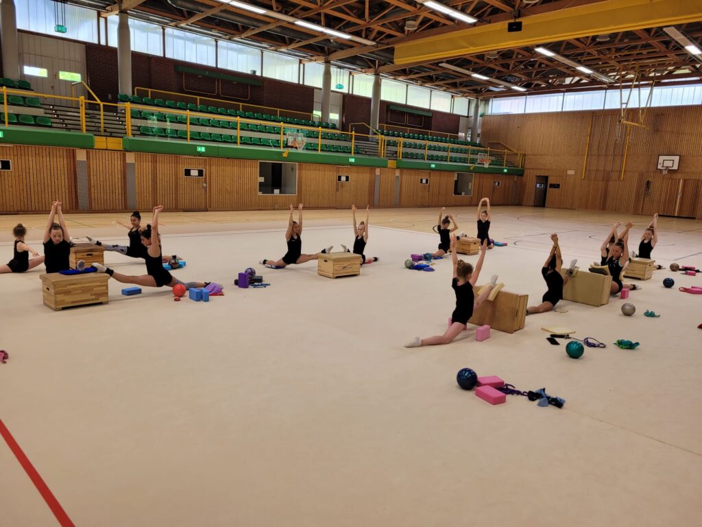 Eine Gruppe von Mädchen macht Dehnübungen in einer Turnhalle.