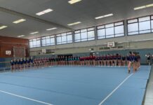 Gruppe von Turnerinnen steht aufgereiht in einer Turnhalle.