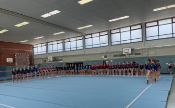 Gruppe von Turnerinnen steht aufgereiht in einer Turnhalle.