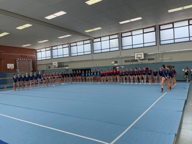 Gruppe von Turnerinnen steht aufgereiht in einer Turnhalle.