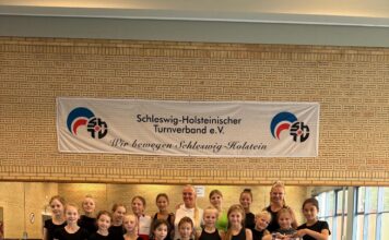 Gruppe in Sportkleidung auf blauer Matte vor einem Banner.