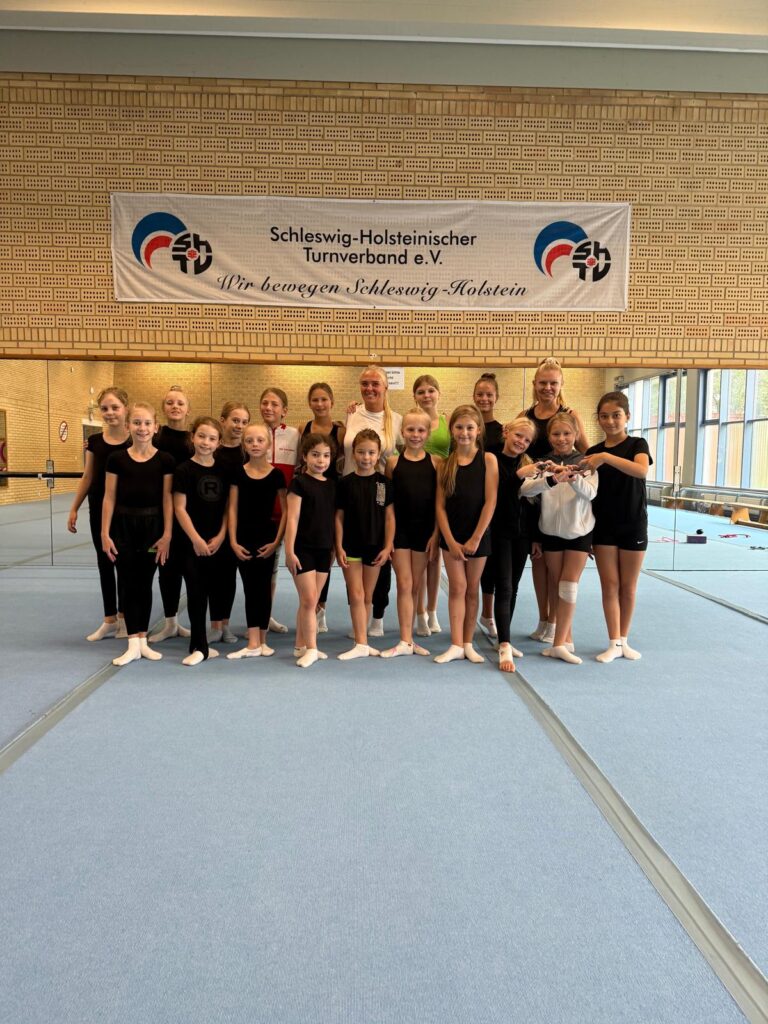 Gruppe in Sportkleidung auf blauer Matte vor einem Banner.