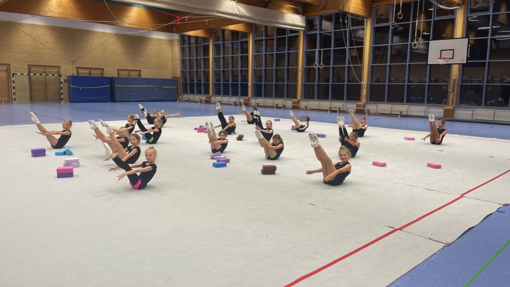 Gruppe macht Gymnastikübungen in einer Sporthalle.