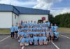 Gruppe in blauen T-Shirts posiert vor einem Gebäude für ein Foto.
