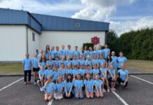Gruppe in blauen T-Shirts posiert vor einem Gebäude für ein Foto.