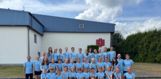 Gruppe in blauen T-Shirts posiert vor einem Gebäude für ein Foto.