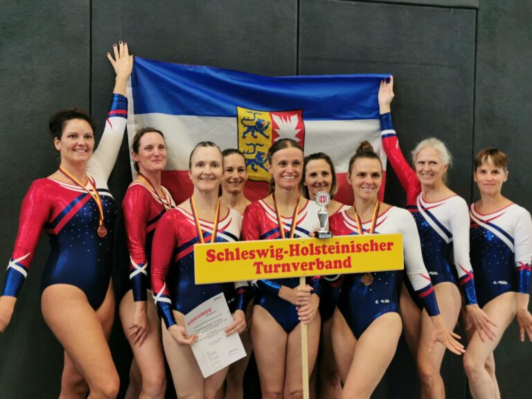 Gruppe von Turnerinnen mit Flagge und Schild des Schleswig-Holsteinischen Turnverbands.
