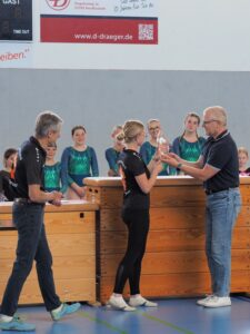 3 Personen vor Turnkasten mit Pokal und Urkunde